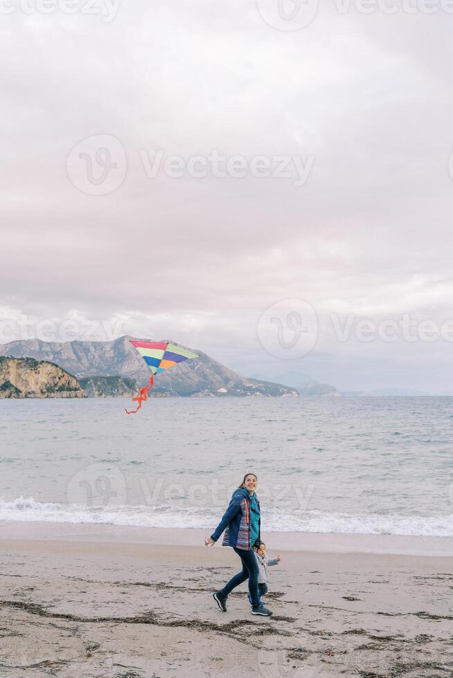 Mom with a little girl walk holding hands along the seashore with a kite on a string photo