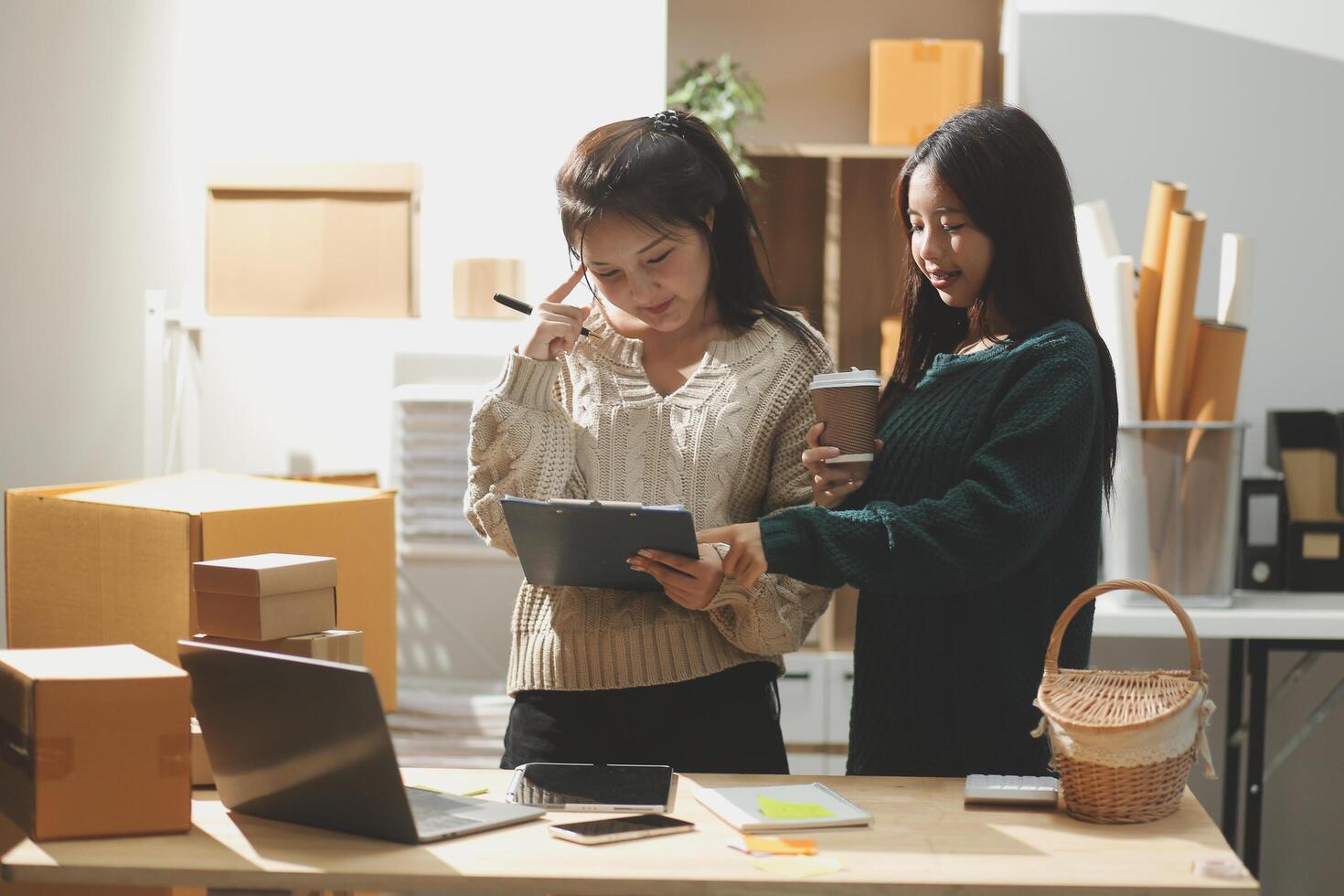 Two women standing in front of a desk with boxes and papers photo