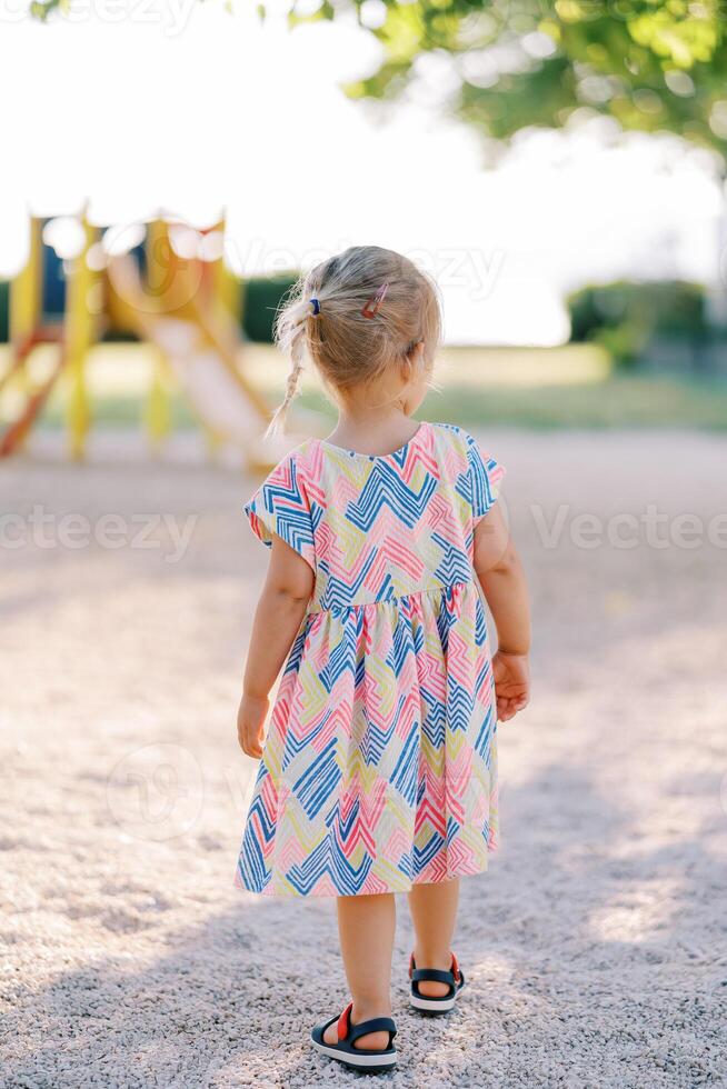 Little girl is walking on the playground. Back view photo