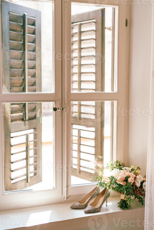 Bride shoes with a bouquet of flowers stand on the windowsill in the room photo