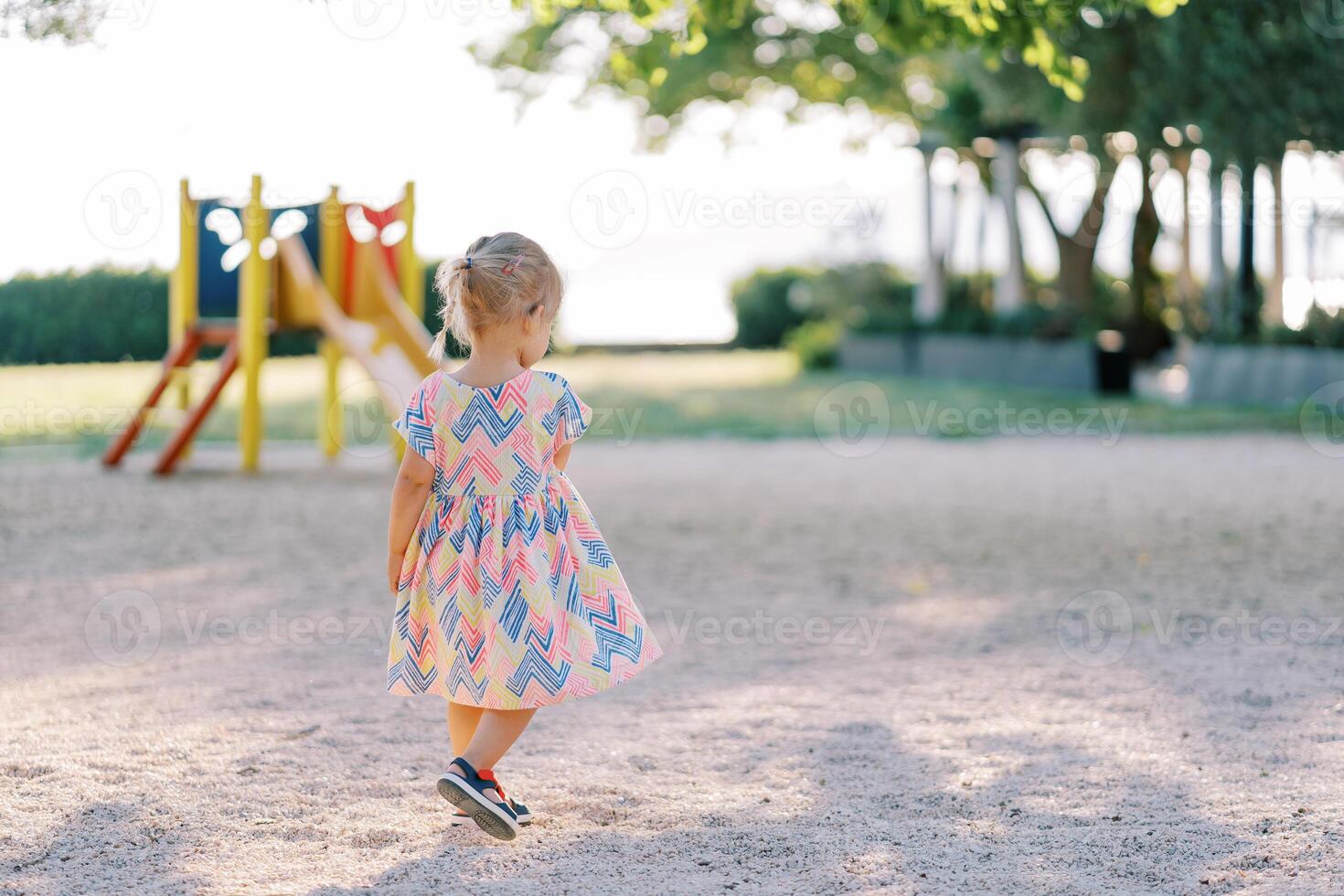 Little girl walks along the playground to a colorful slide. Back view photo