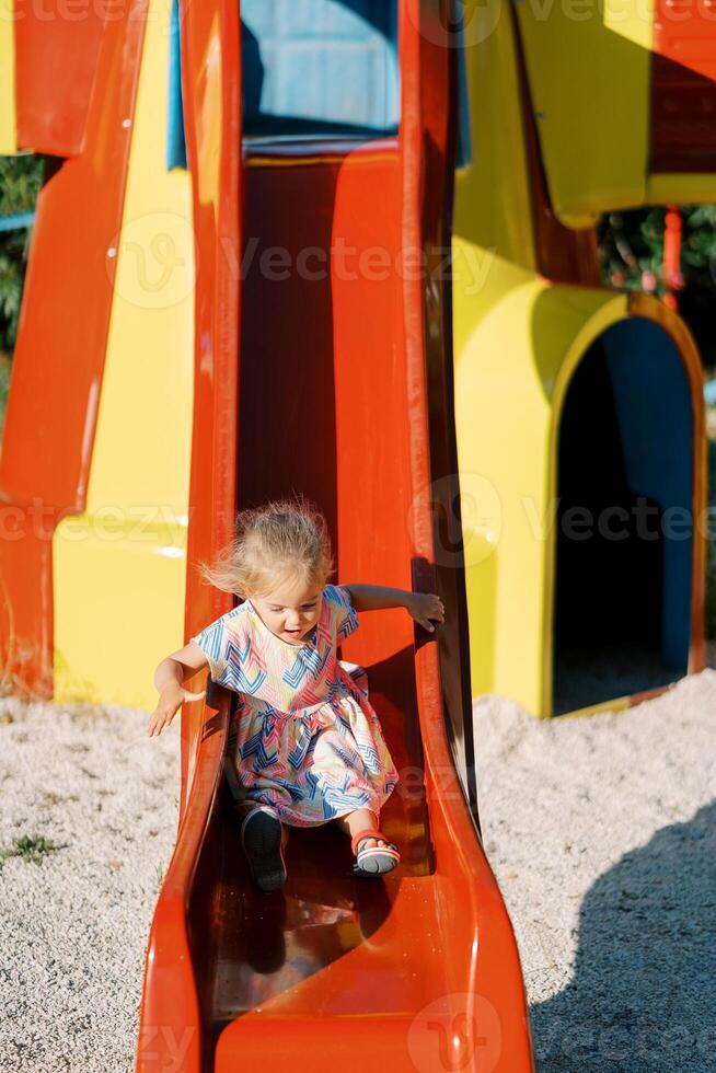 Little girl with flying hair slides down a slide holding onto a handrail photo