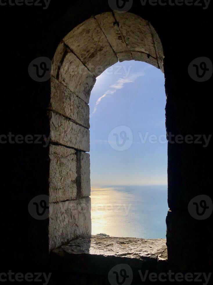 Sea view through the oval window of the stone tower. Sea surface illuminated by the evening sun. photo