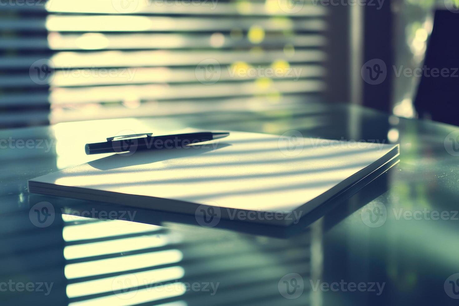 Pen and notebook on glass table with striped shadow patterns from blinds photo