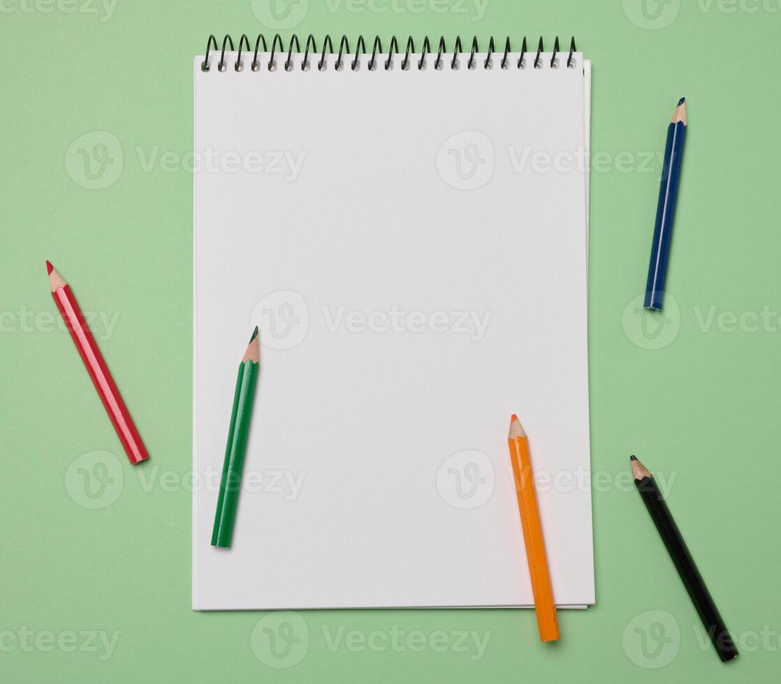Open notebook with white blank sheets and wooden pencils on green background, top view photo