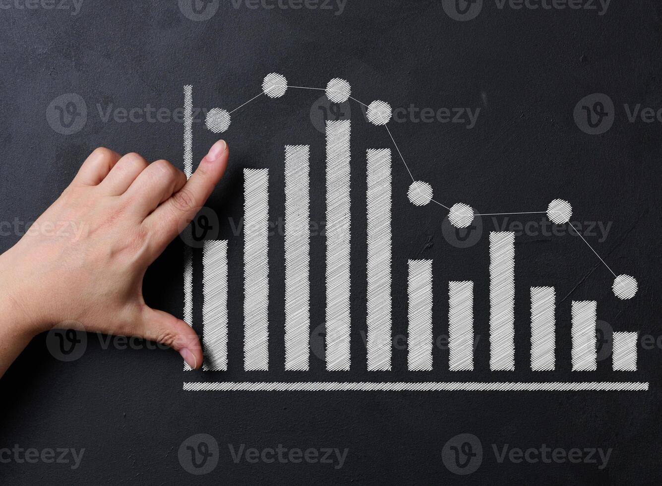 A hand interacts with a bar and line graph drawn in white chalk on a blackboard. photo