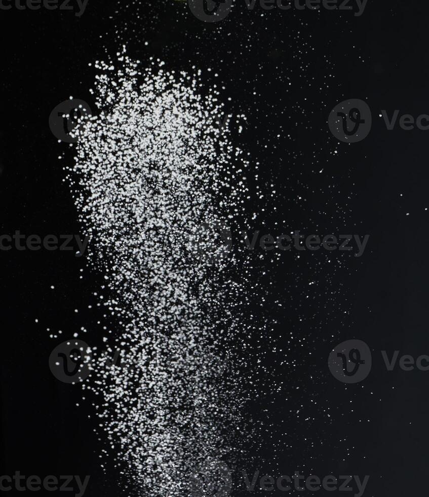 Close-up of white granular particles sugar, falling against a black background. High contrast and detailed texture of the grains photo