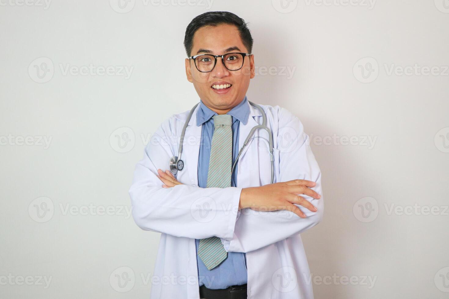 A man in a white lab coat is smiling and holding a stethoscope. Concept of professionalism and confidence, as the man is posing for a picture while wearing his medical attire photo