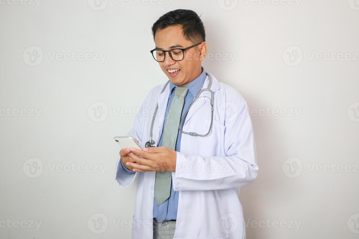 Good looking Indian male doctor using speaking over or presenting Smartphone, standing isolated over white background. photo