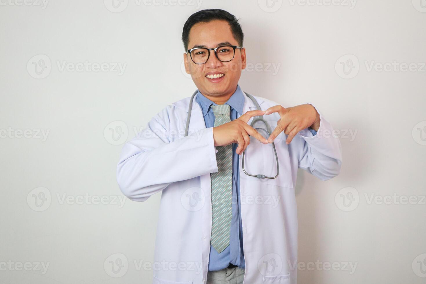 Portrait of Middle aged, handsome, Asian, doctor, on duty at hospital stethoscope around his neck, proudly making heart shape sign for love and support, on isolated white background photo