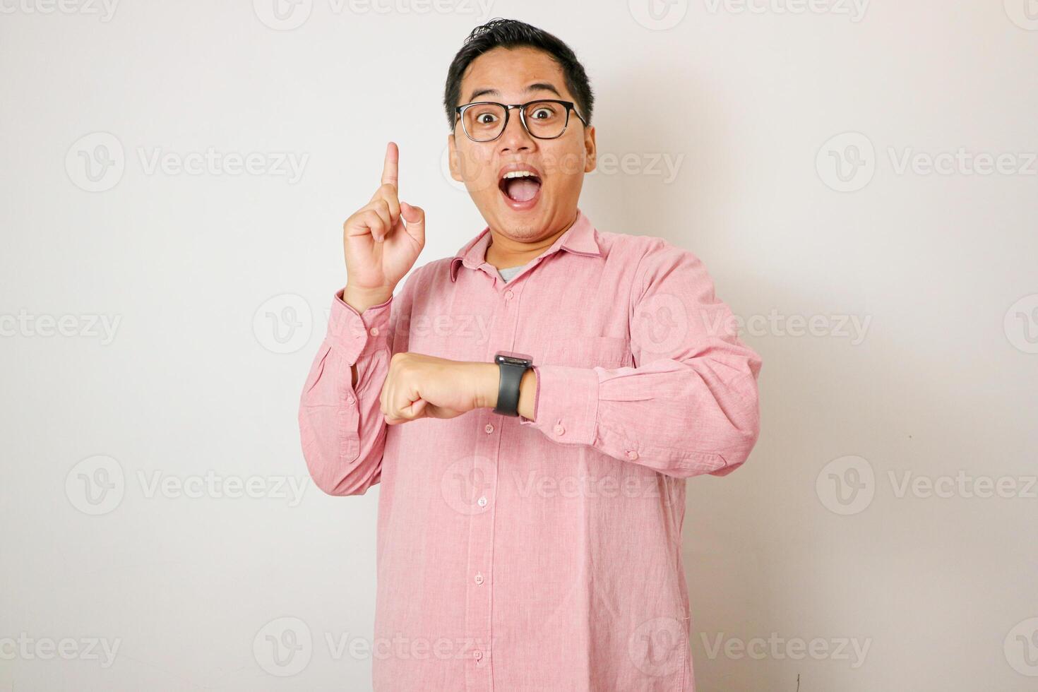 Adult Asian man pointing forward with happy expression while showing his watch photo