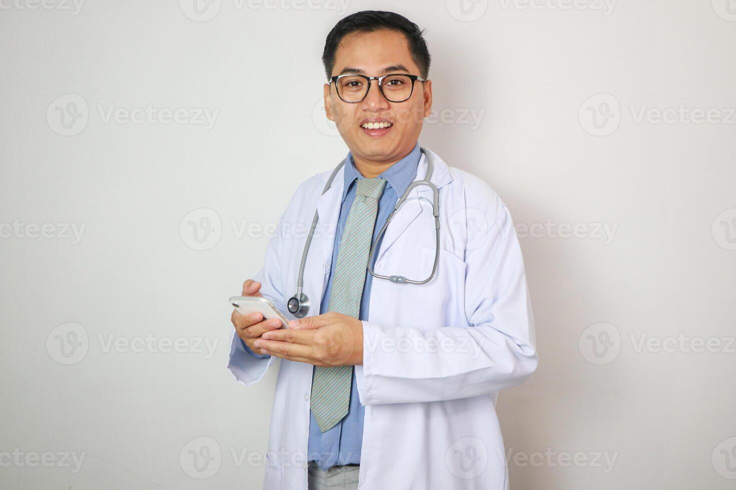 asian man in white coat showing his phone. he is smiling and he is in a lab photo