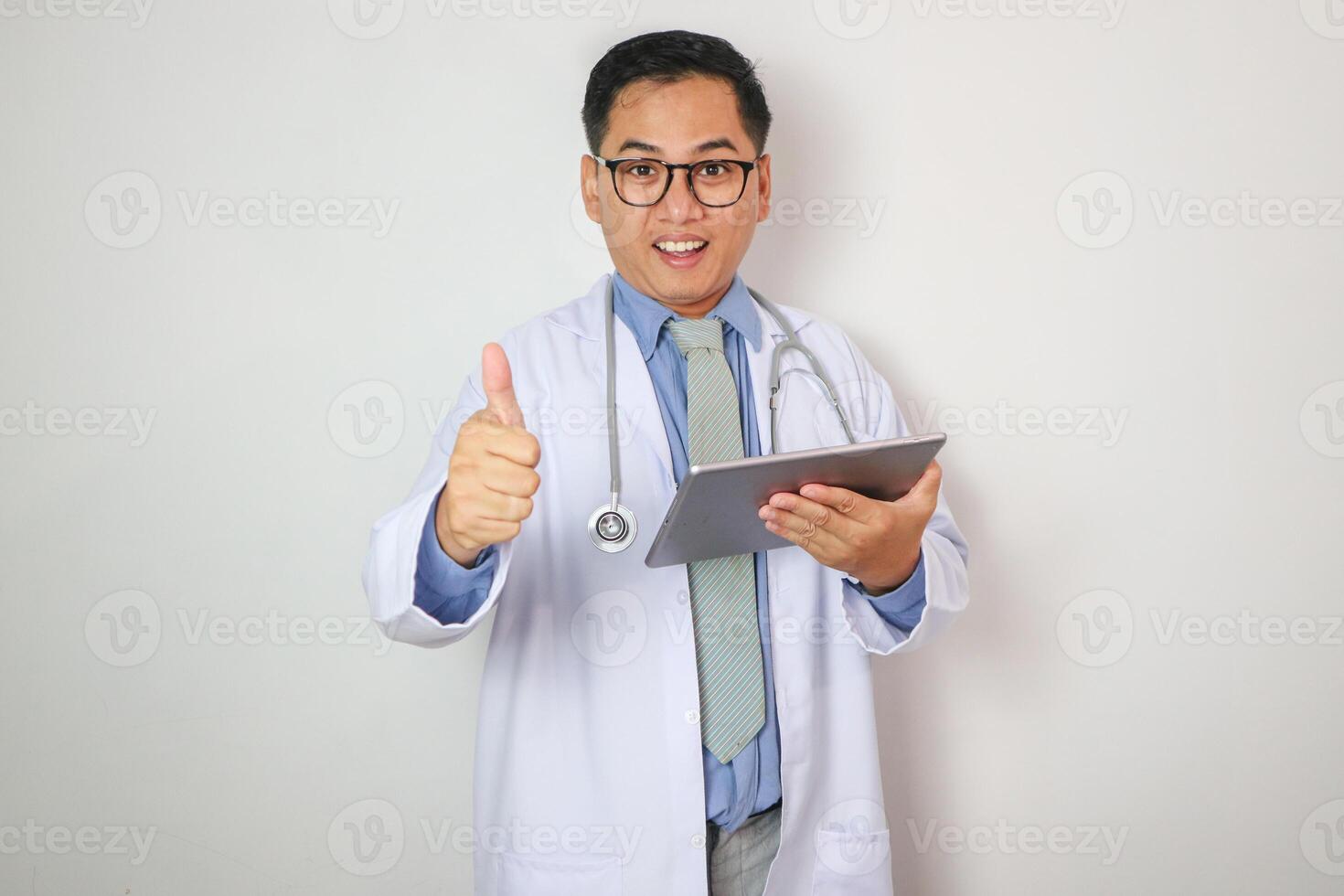 Portrait of Asian mature doctor standing in white lab coat and smiling at camera while holding tablet pc and showing thumb up photo