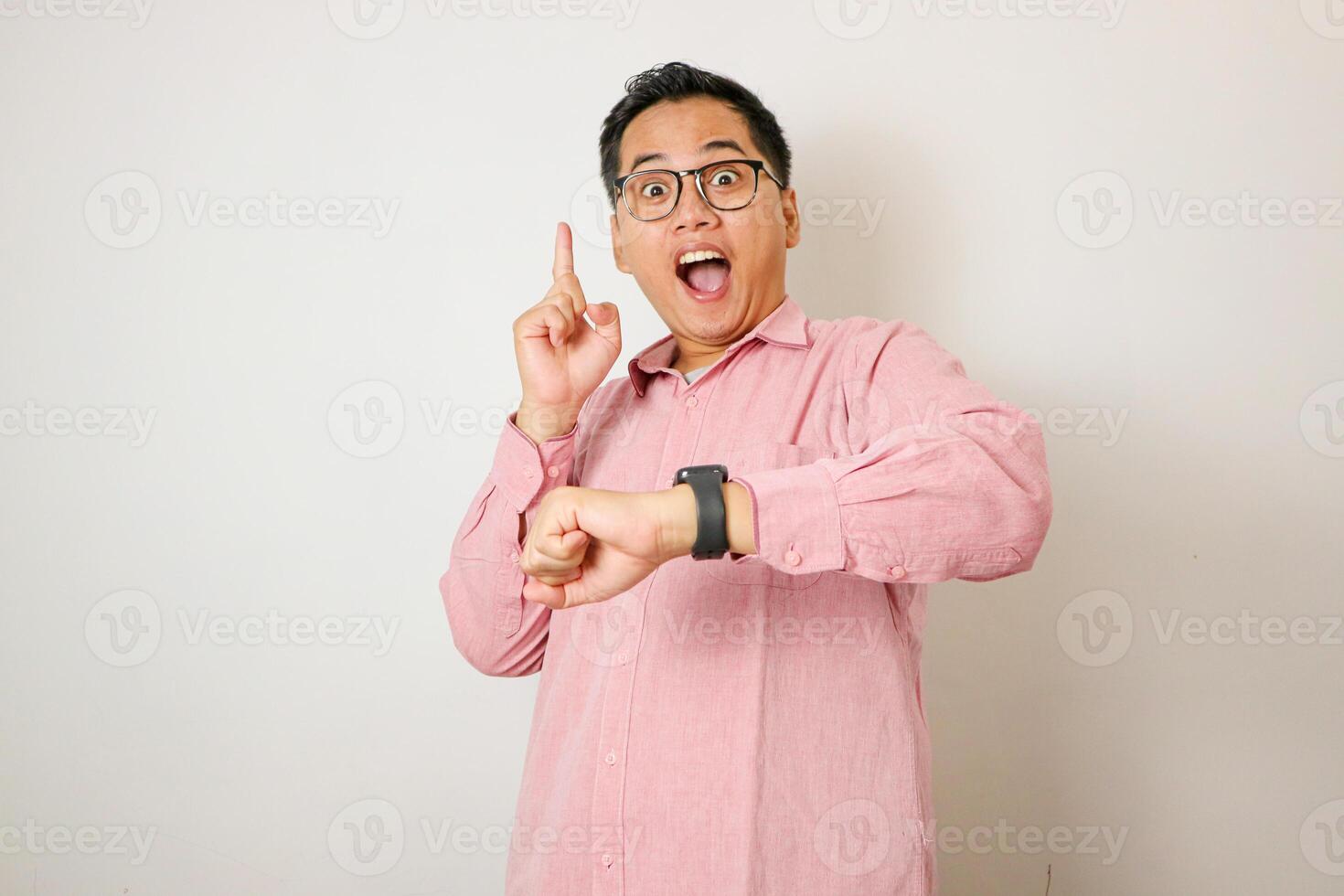 A young Asian man, wearing a white shirt and black watch, looks thoughtfully upward while pointing with his right index finger. The plain white background highlights the subject's contemplative photo