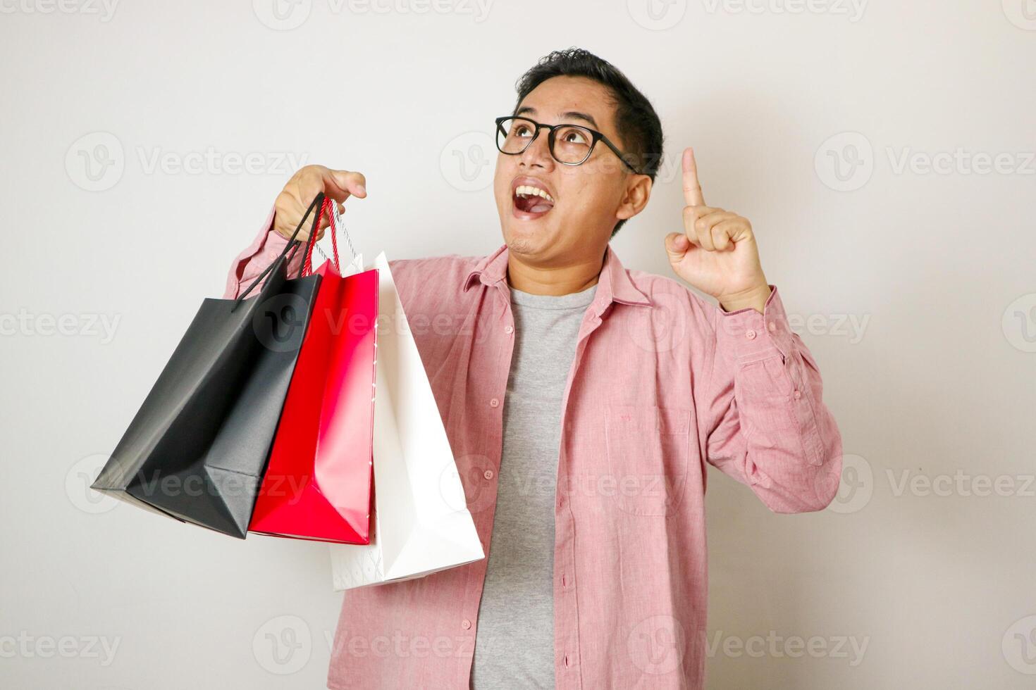 Portrait of young Asian man holding a shopping bag and pointing up on a white background photo