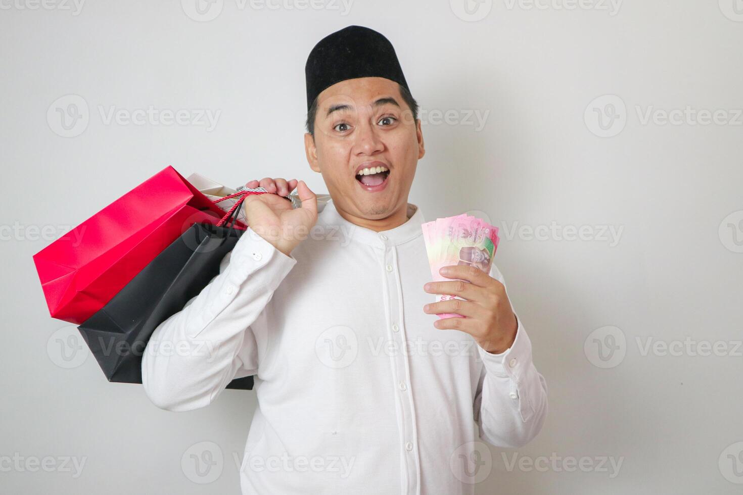 Full Body Of Smiling Young Asian Man Wearing Muslim Clothes Showing Shopping Bag and money To Front Isolated On white Background photo