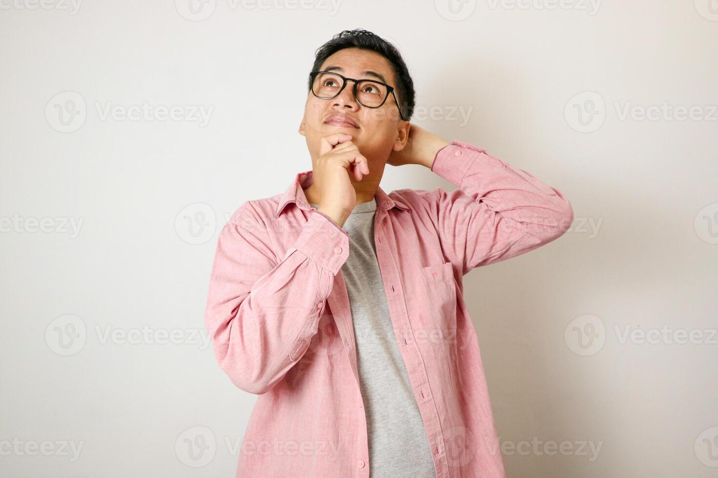 Good Offer. Portrait of pensive asian man in glasses looking up at copy space, touching his chin, isolated over white studio background. Thoughtful teen guy thinking and making decision photo