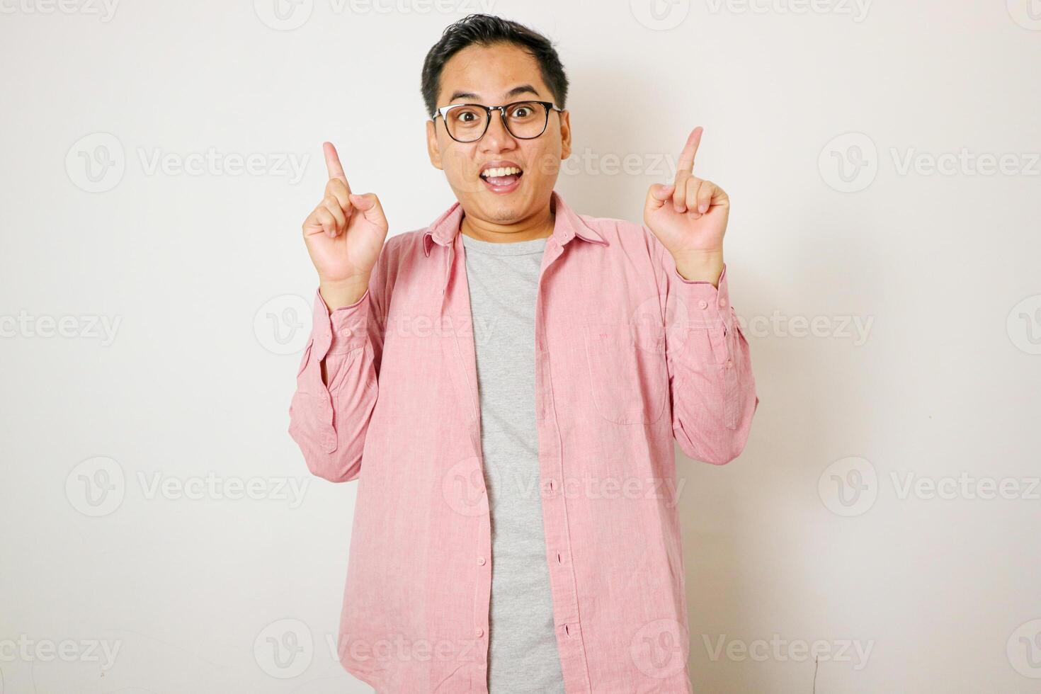 Happy handsome smiling young Asian man with hands poiting up to empty space above photo
