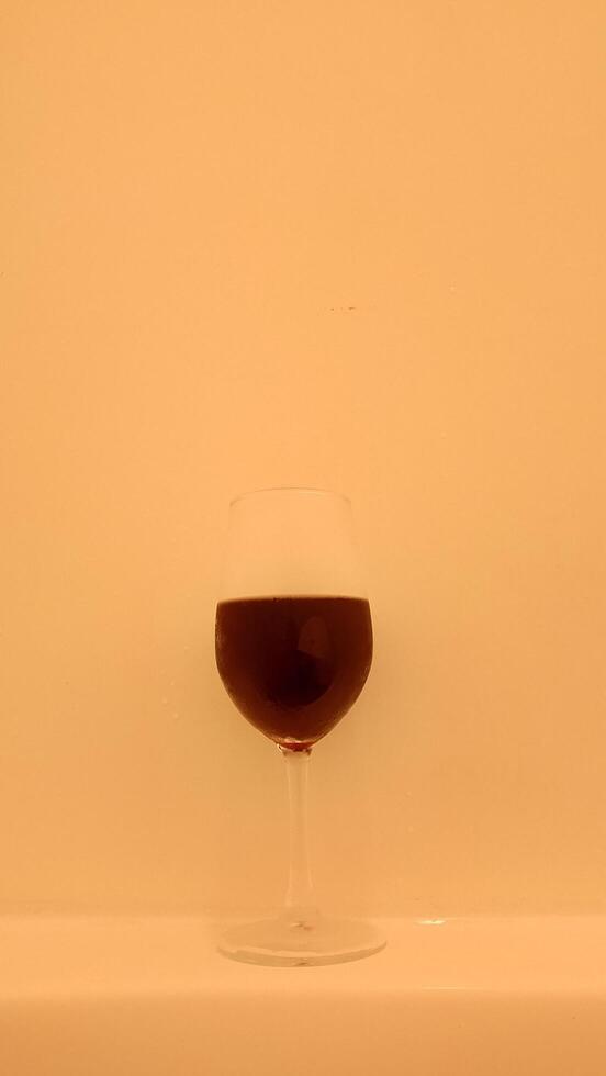 A glass of wine sitting on a table in front of a white wall photo