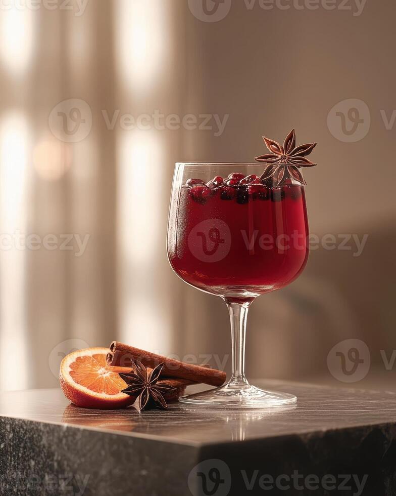 A glass of red beverage garnished with spices and orange on a table. photo