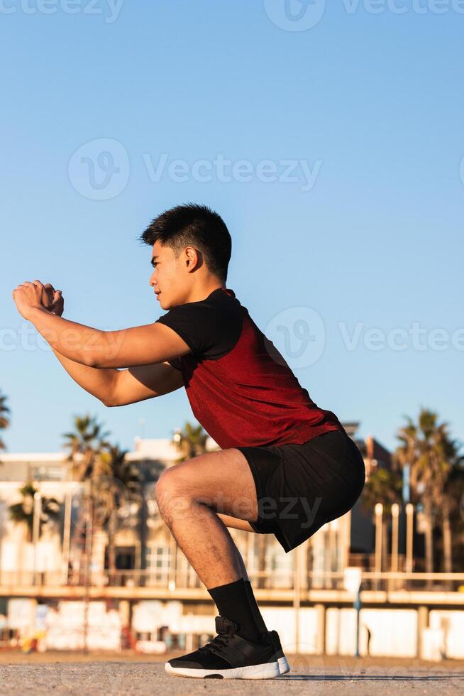 Ethnic sporty man doing lunges in the beach photo