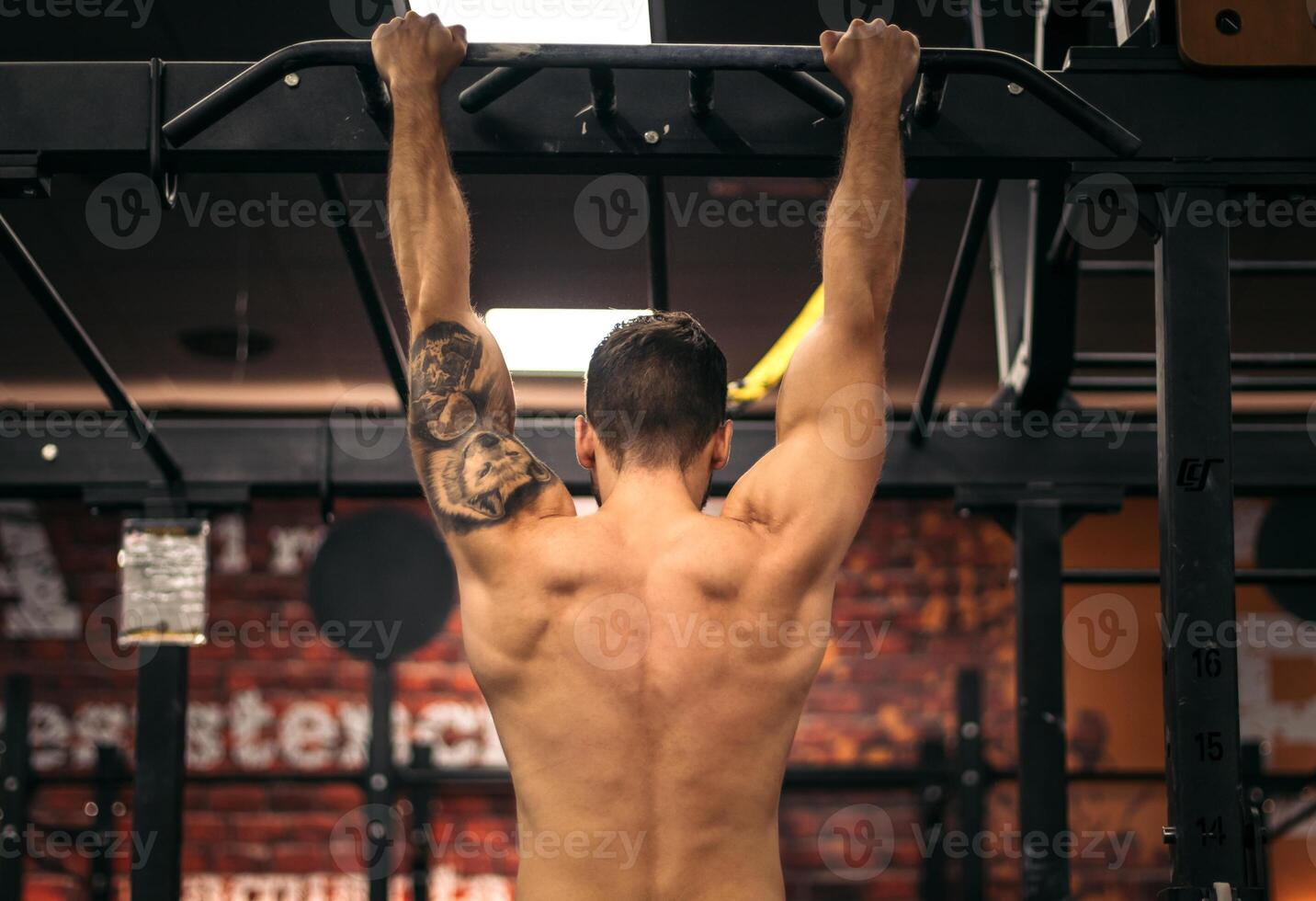 back view of a strong man doing pull ups in a gym photo