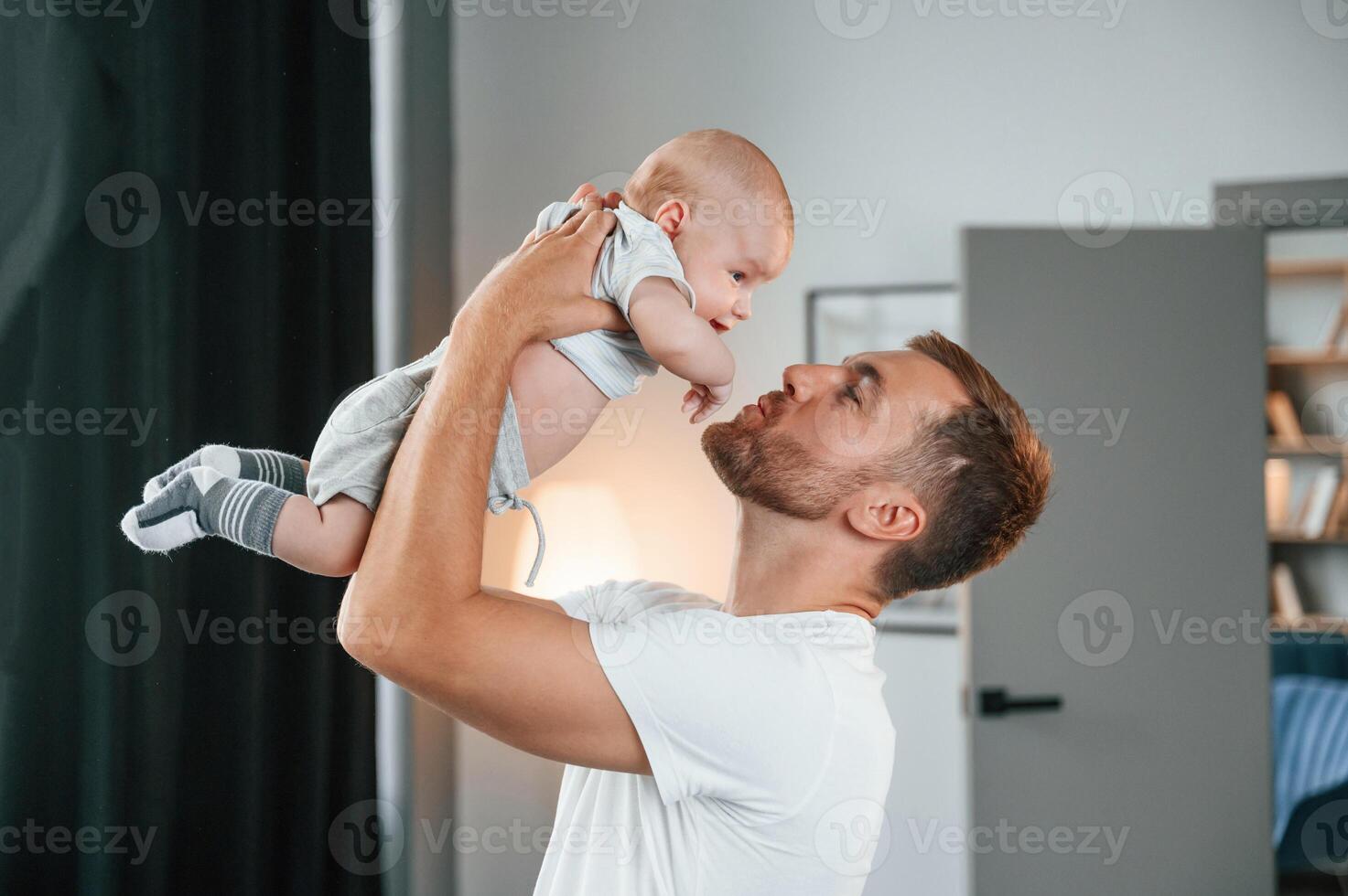 With baby in hands. Smiling, having fun. Father with toddler is at home, taking care of his son photo