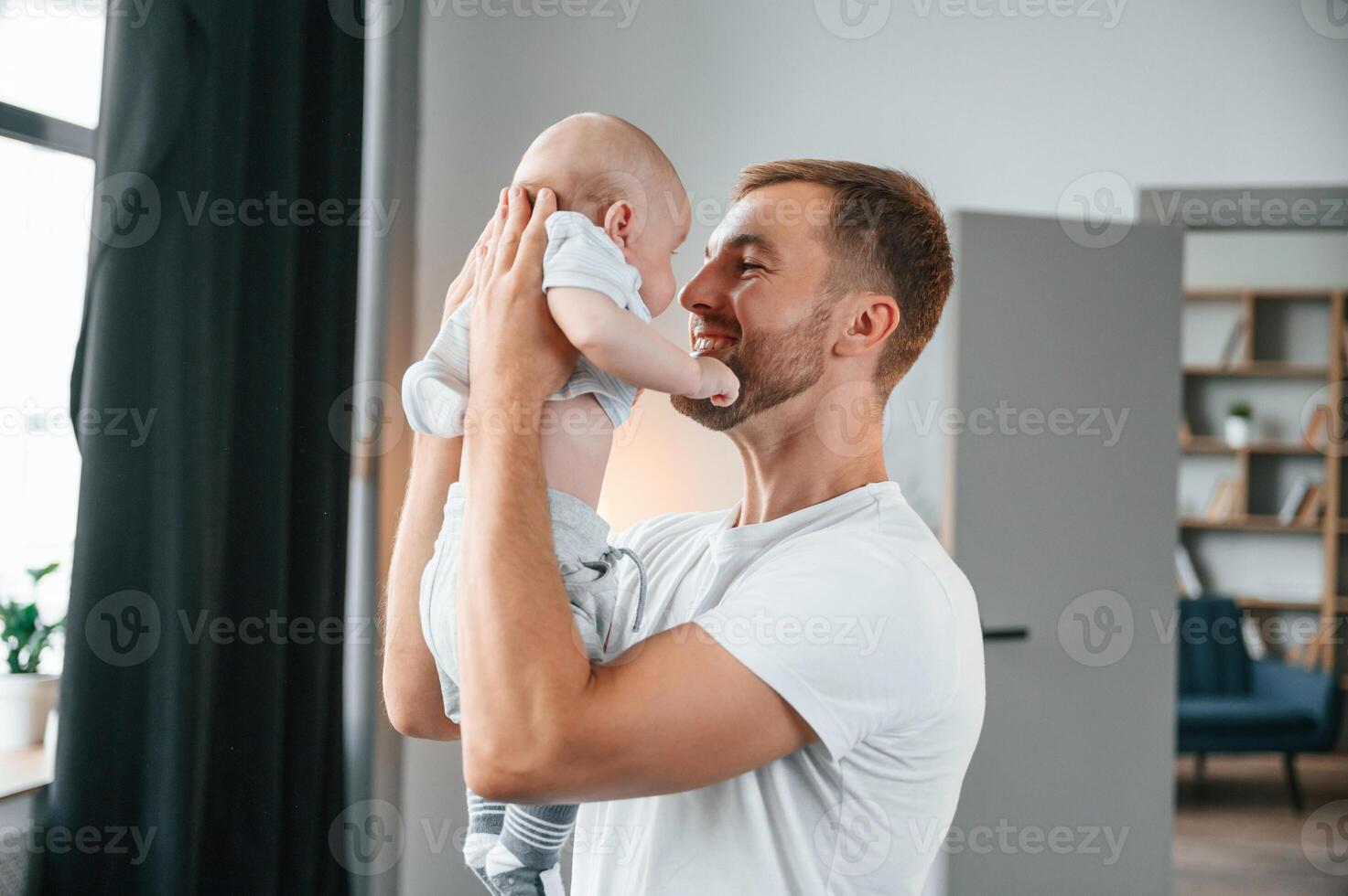 Smiling, having fun with baby is ,in the hands. Father with toddler is at home, taking care of his son photo