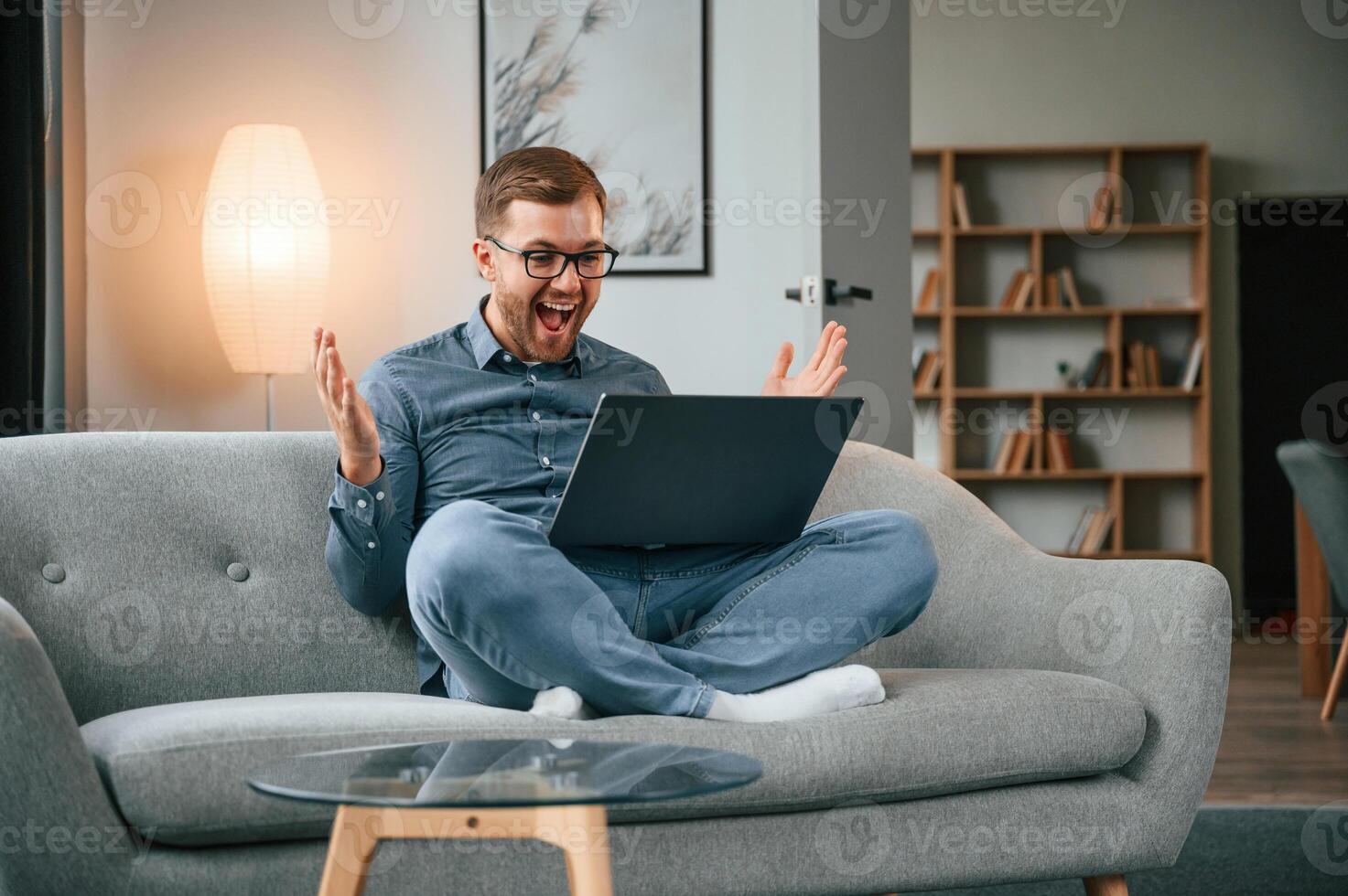 Celebrating succes.s. Male freelance worker is using laptop at home. Cozy apartment photo