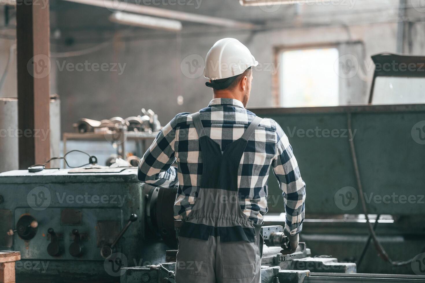 Rear, view. Operating machine. Factory male worker in uniform is indoors photo