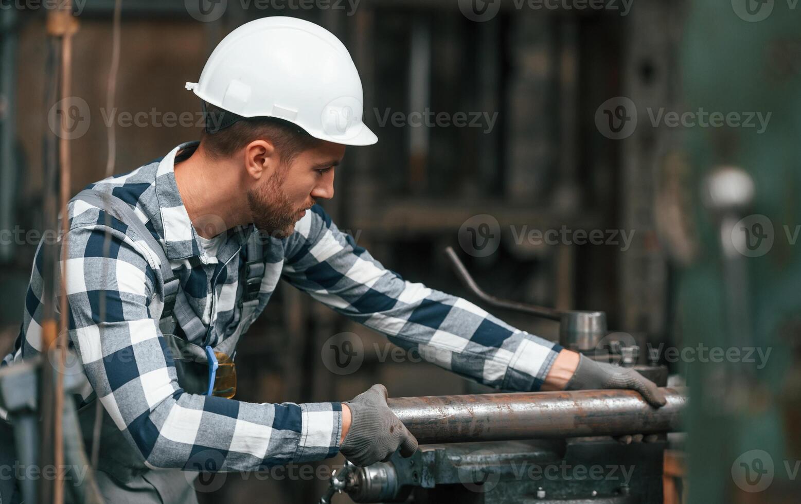 Working, ,by operating machine. Factory worker in uniform is indoors photo