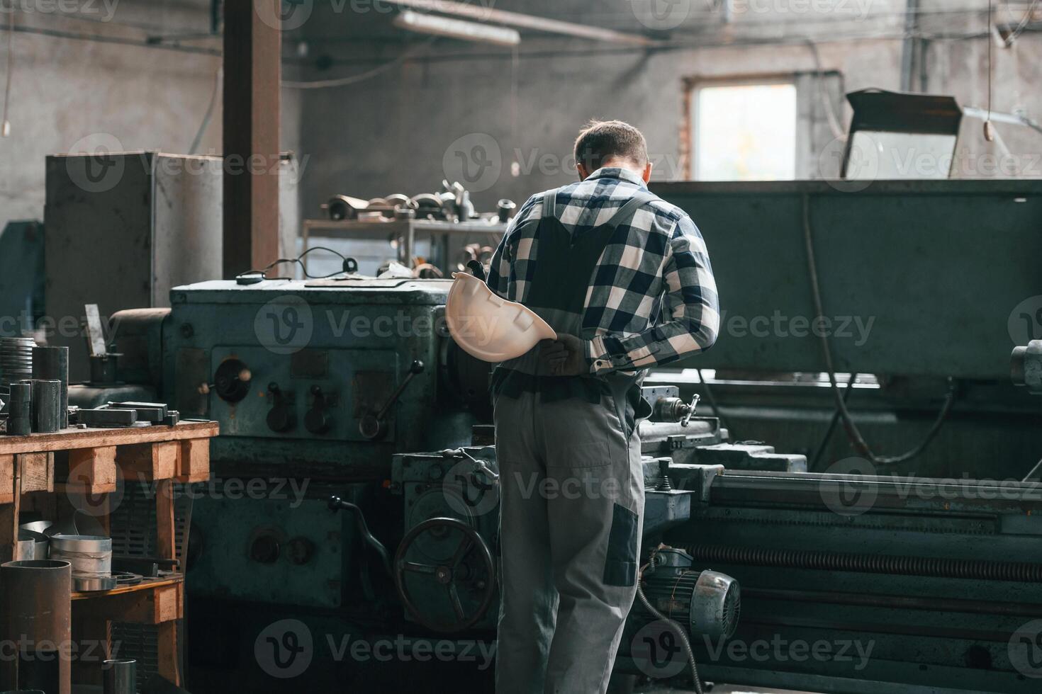 Rear view. Operating machine. Factory male worker in uniform is indoors photo