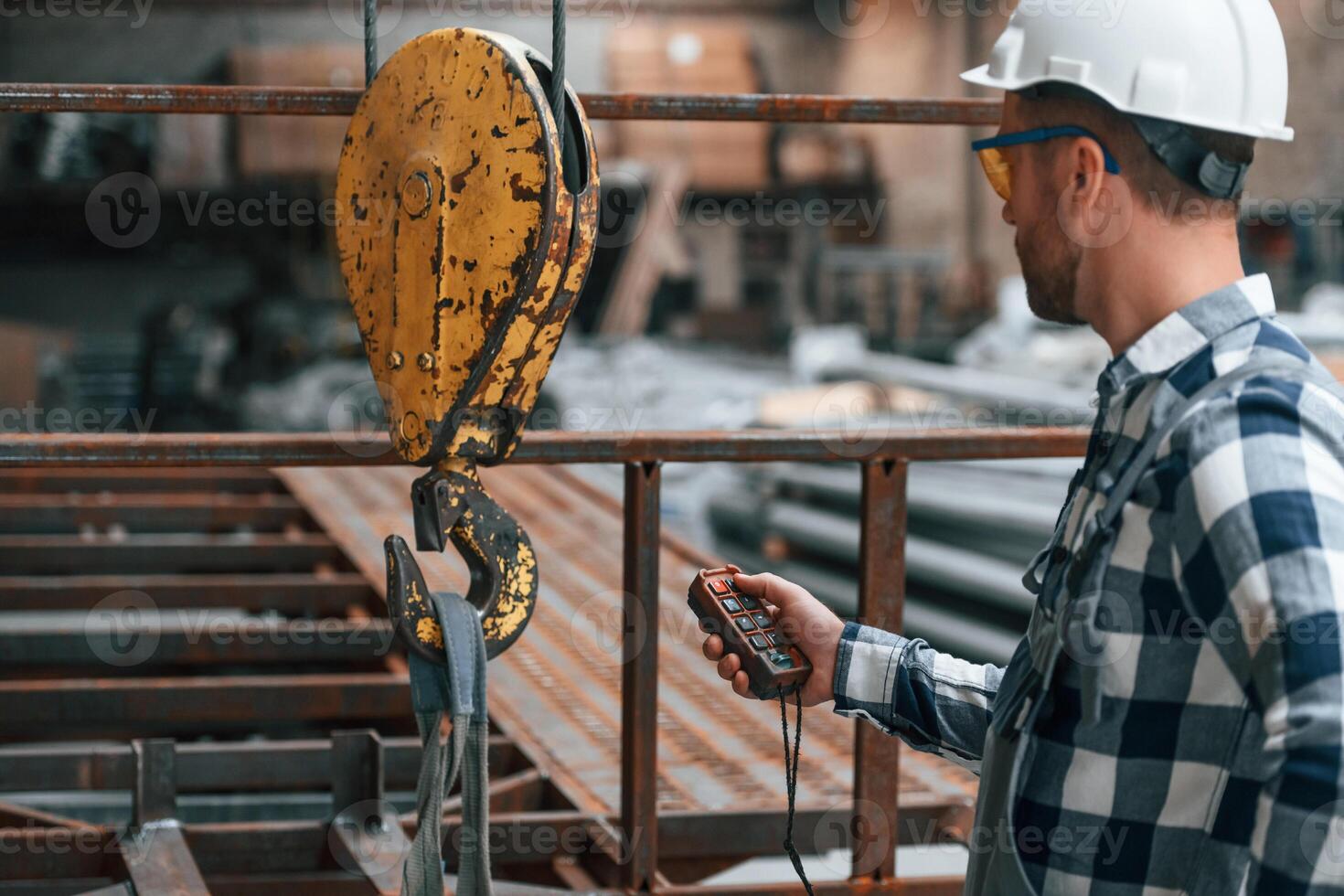 Using the controller, with buttons to operate the little crane machine. Factory male worker in uniform is indoors photo