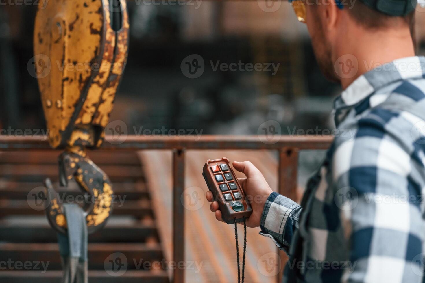 Using the controller with buttons to operate the little crane machine. Factory male worker in uniform is indoors photo