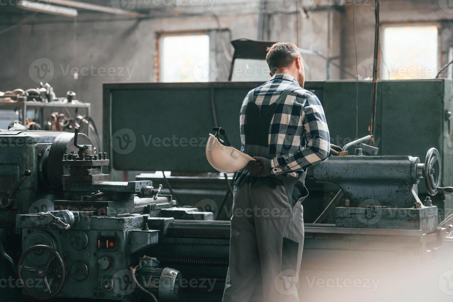Rear view... Operating machine. Factory male worker in uniform is indoors photo