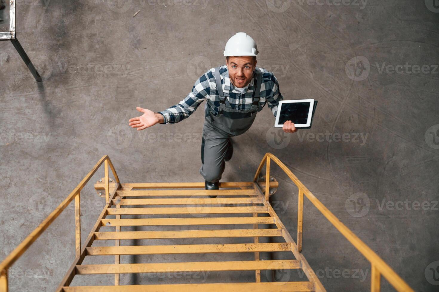 View from the top of ladder.. Factory male worker in uniform is indoors photo