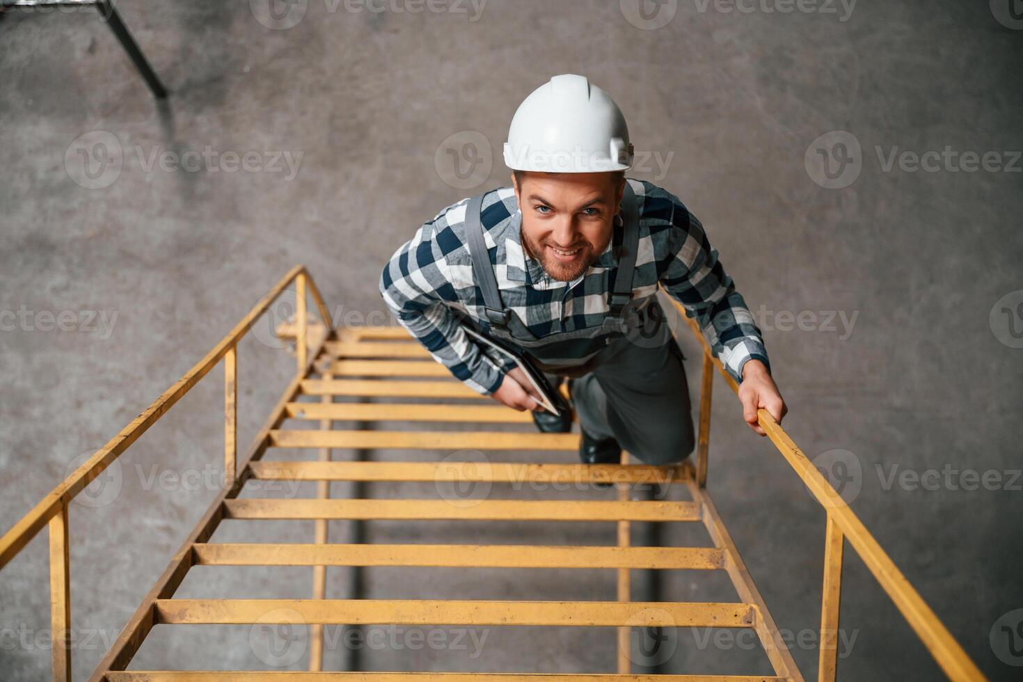 Top view. Going up on the ladder. Factory male worker i,n uniform is indoors photo