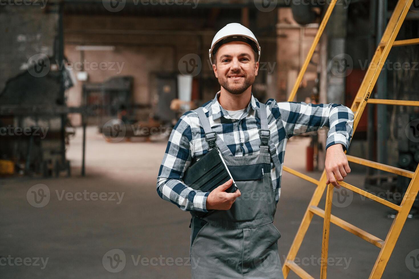 Leaning on the ladder.. Factory male worker in uniform is indoors photo