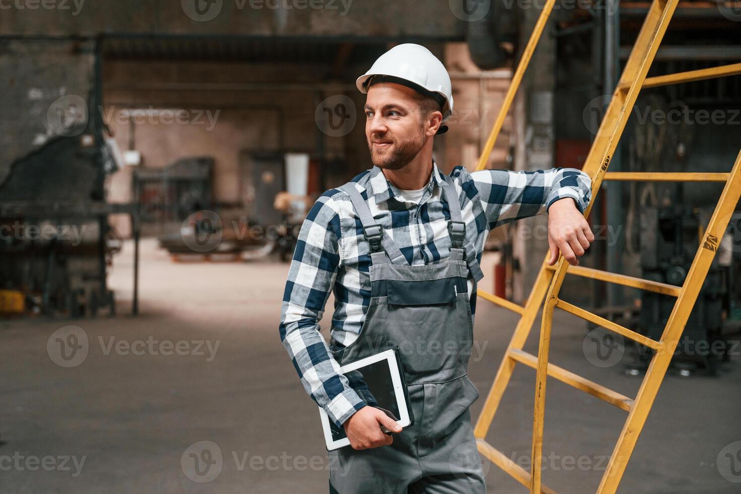 Leaning on the ladder. Factory male, worker in uniform is indoors photo