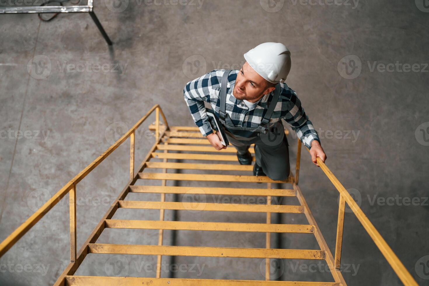 Top view. Going up on the ladder.. Factory male worker in uniform is indoors photo