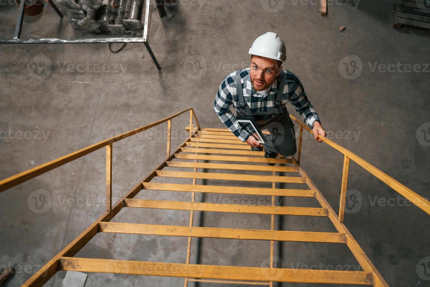 Top view. Going up on the ladder. Factory male, worker in uniform is indoors photo