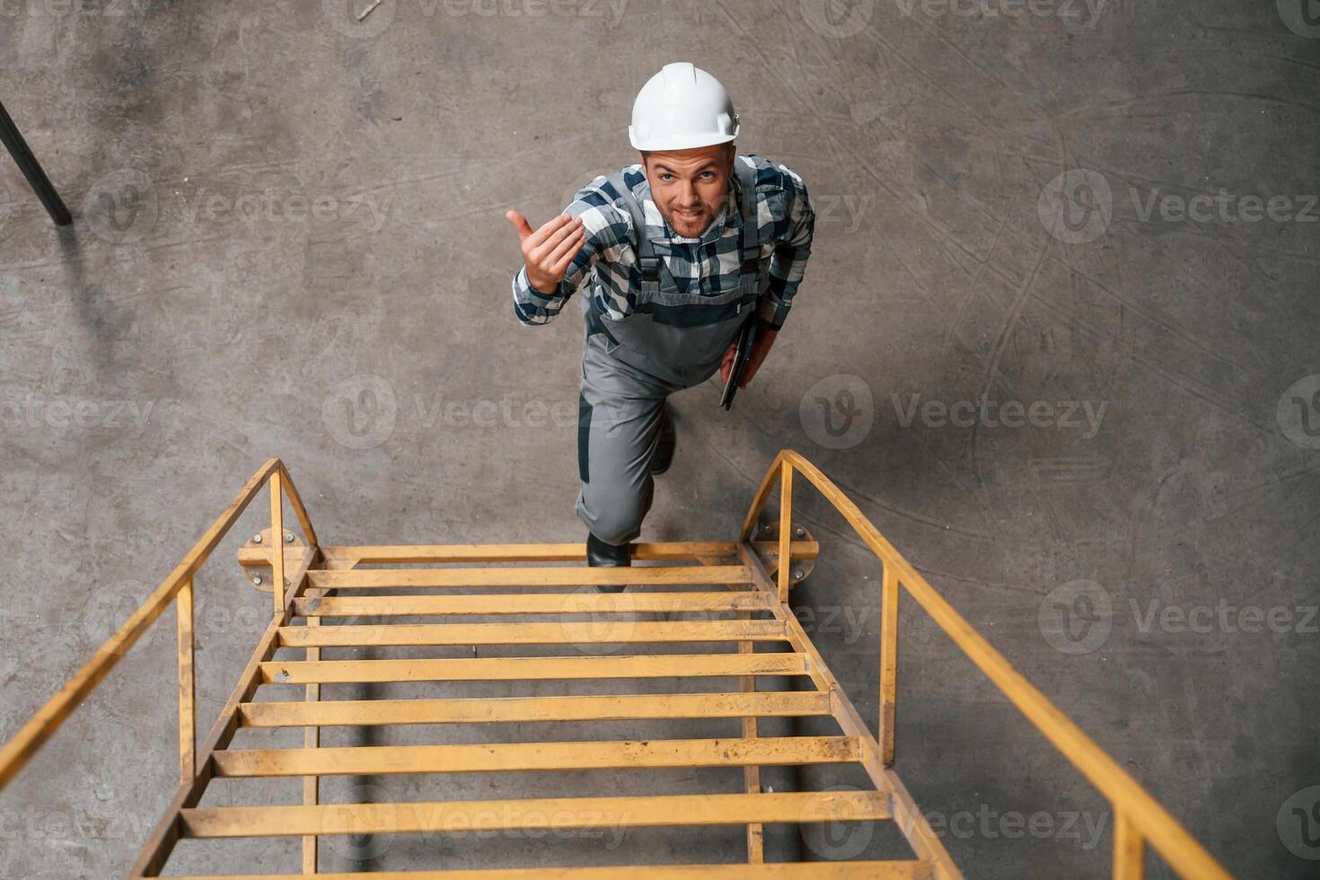 View from the top of ladder. Factory male worker in uniform is indoors photo