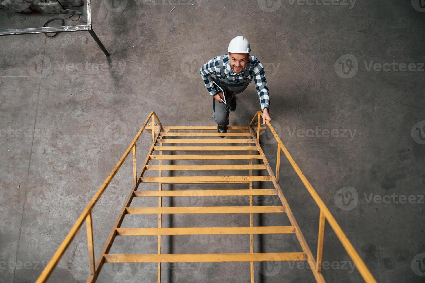 View from the, top of ladder. Factory male worker in uniform is indoors photo