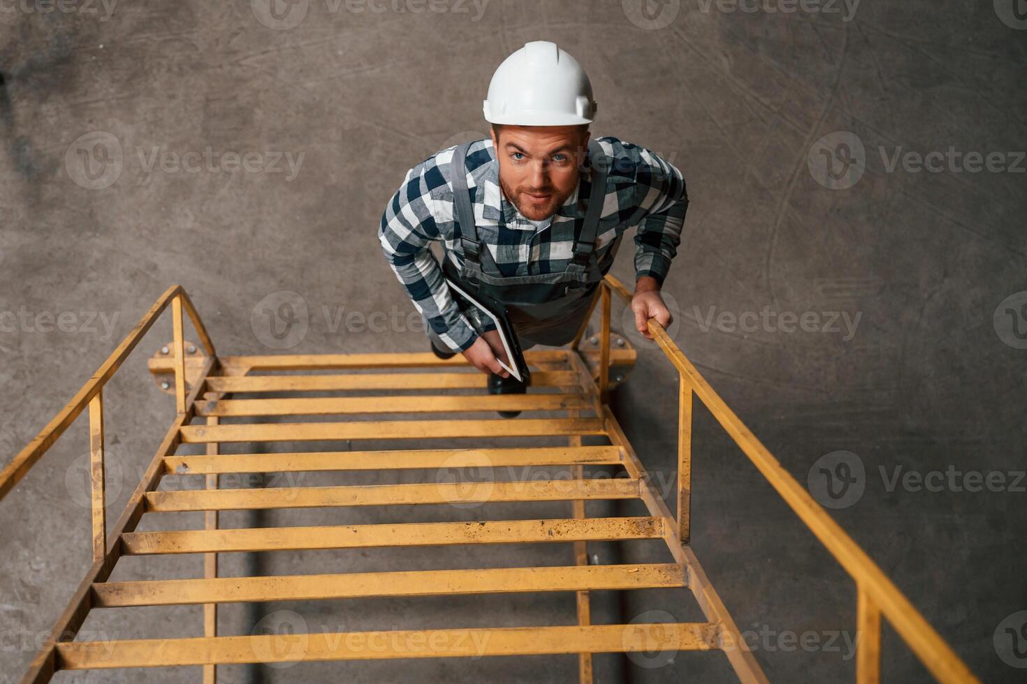 Top ,view. Going up on the ladder. Factory male worker in uniform is indoors photo