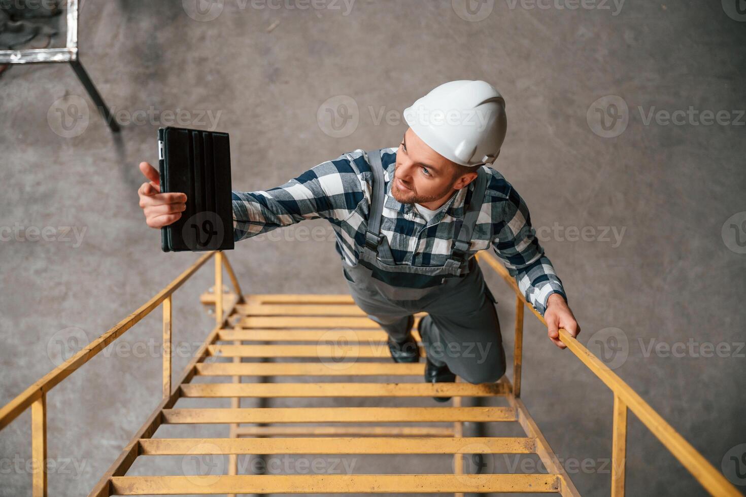 Top view. Going up on the ladder. Factory male ,worker in uniform is indoors photo