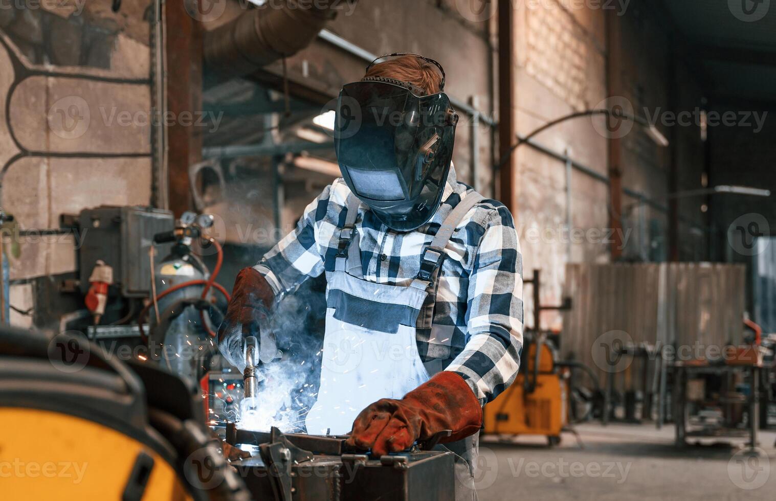 In ,protective mask. Welding the iron. Factory male worker in uniform is indoors photo