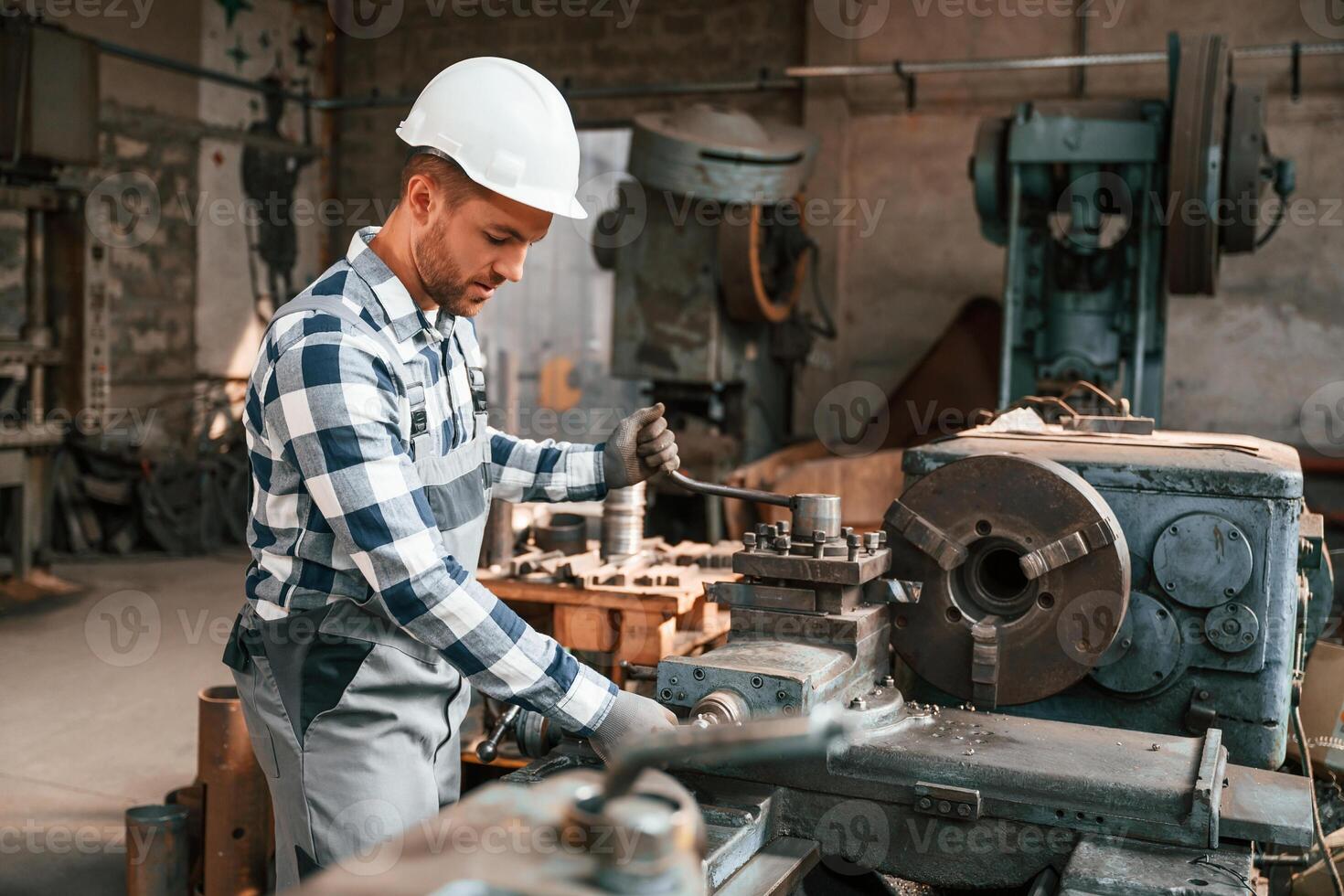 Side view. Operating the machine. Factory male worker in uniform is indoors photo