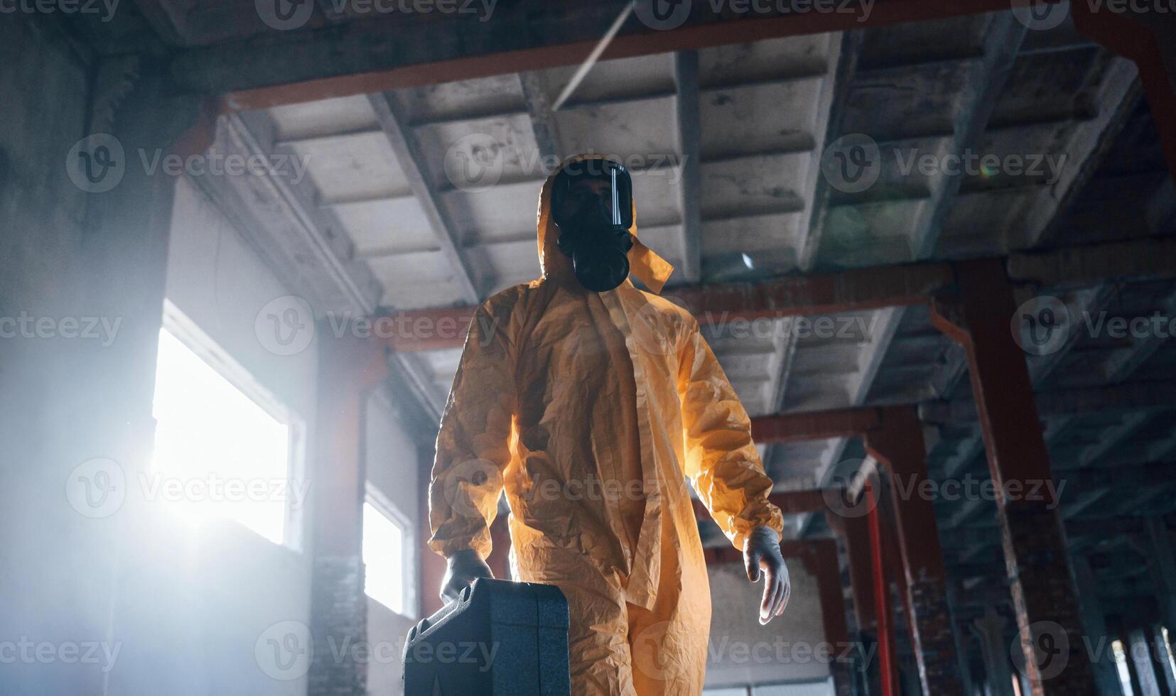 Walking with hard ,case. Man dressed in chemical protection suit in the ruins of the post apocalyptic building photo