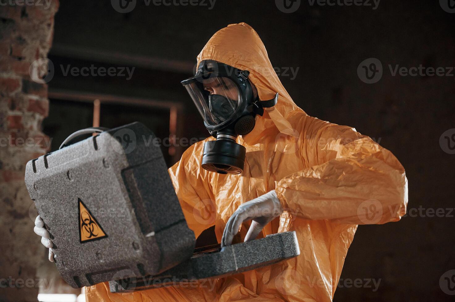 Sitting, with radioactive case. Man dressed in chemical protection suit in the ruins of the post apocalyptic building photo