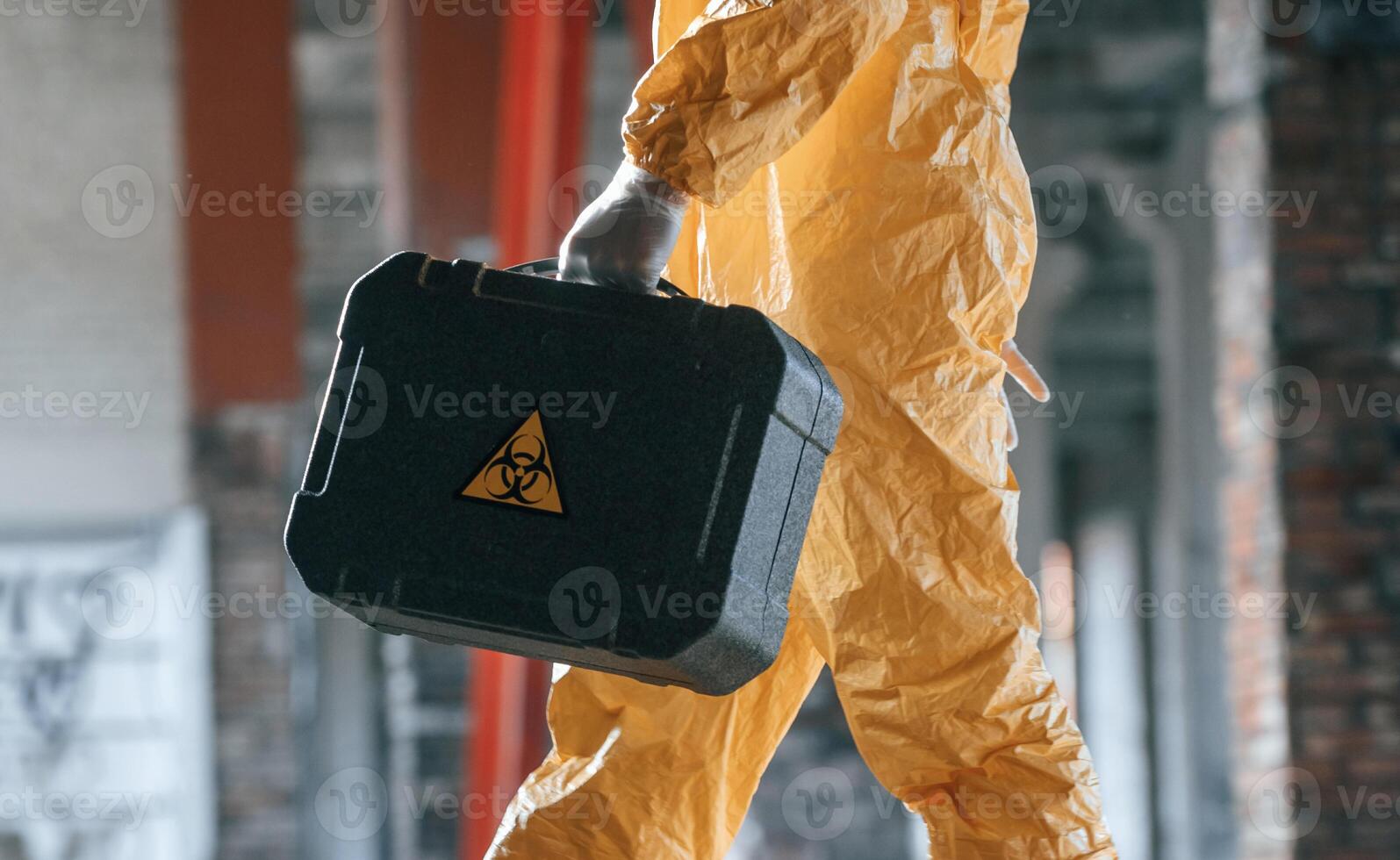 The case with ,biohazard sign on it. Man dressed ,in chemical protection suit in the ruins of the post apocalyptic building photo